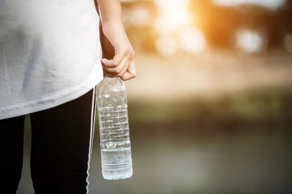 Rainwater marka su şişesi tutan sporcu, sabah güneşi arka planda, açık hava sporları için ideal su çözümü.